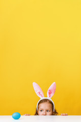 Cute little child girl with bunny ears at home is hunting for Easter eggs.