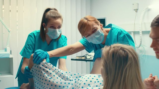 In the Hospital Woman Giving Birth, Husband Holds Her Hand in Support, Obstetricians Assisting