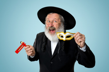 Portrait of a senior orthodox Hasdim Jewish man with wooden Grager Ratchet at Jewish festival of...