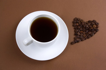 top view of black coffee cup and heart with coffee beans on brown background