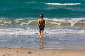 the child stands in the sea in front of the waves