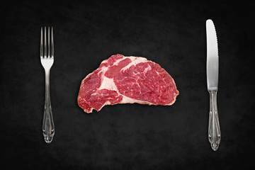  raw steak / red meat with knife and fork on black background -