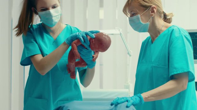 In the Hospital Woman in Labor Pushes and Gives Birth, Baby Comes out, Obstetricians Assist Delivery, Husband Supports His Wife. Close-up Footage