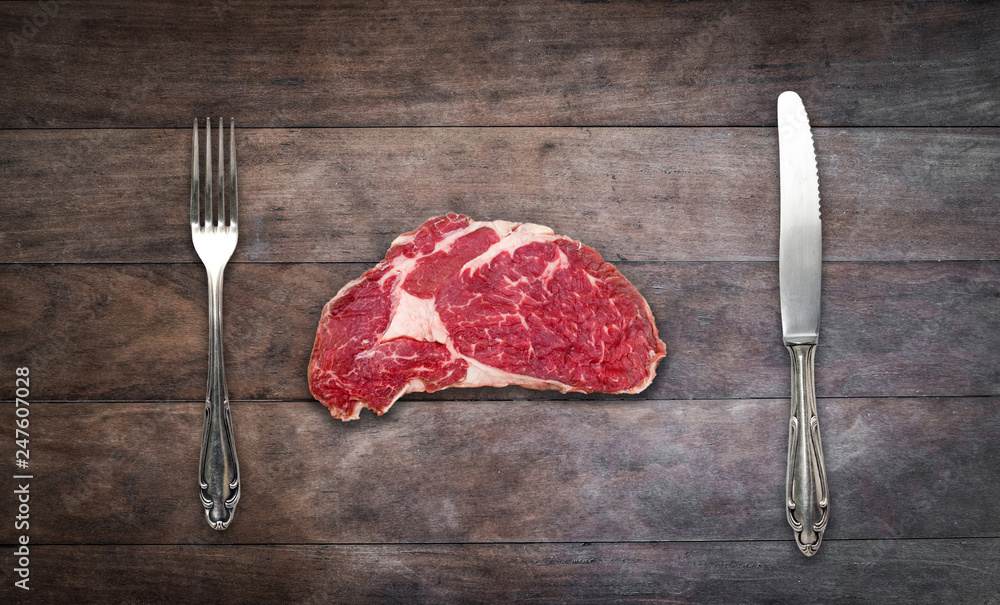 Wall mural slice red meat / raw steak with knife and fork on wooden background