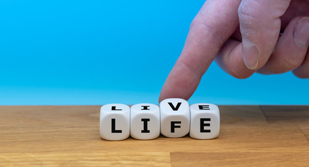 Hand turns a dice and changes the word "LIVE" to "LIFE".