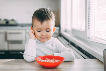 A child in the kitchen eating their own oatmeal with a red plate