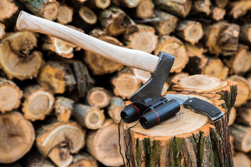 axe, binoculars and jackknife case on the stump, firewoods on the background