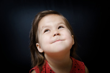 Child looking up on dark background. little girl smiling and looking at something amazing