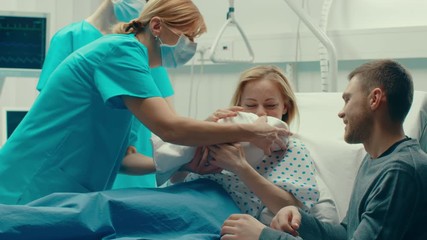 In the Hospital Woman in Labor Pushes and Gives Birth, Baby Comes out, Obstetricians Assist Delivery, Husband Supports His Wife. Side View Footage. 