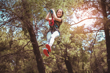 Happy school girl enjoying activity in a climbing adventure park on a summer day