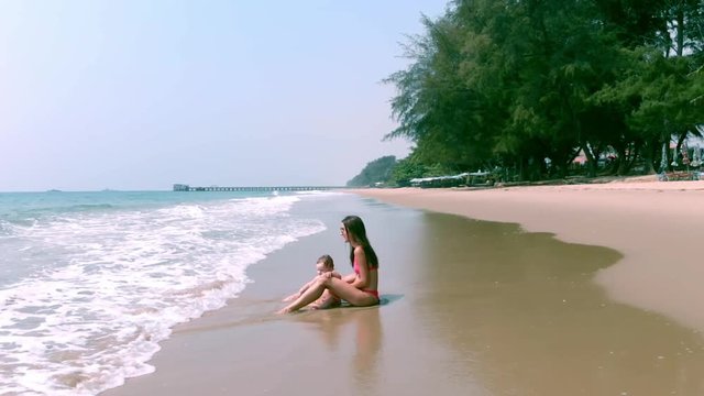 Mom and girl playing on the beach of the sae sit, walk and swim. Mom and daughter are sitting in the sea and watching the waves.