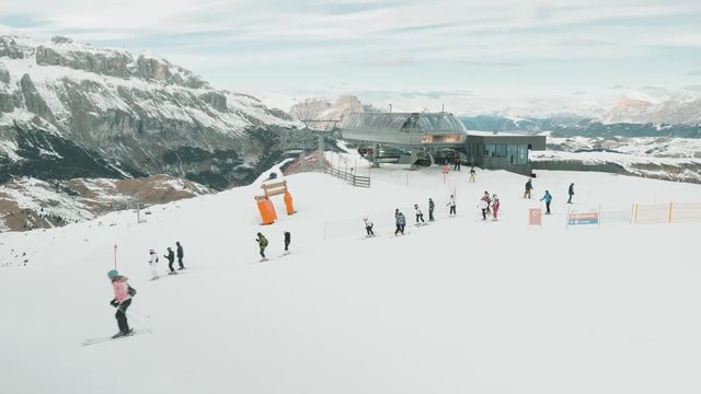 Large group of skiers exiting ski lift to head downhill as other skiers pass across in frame.