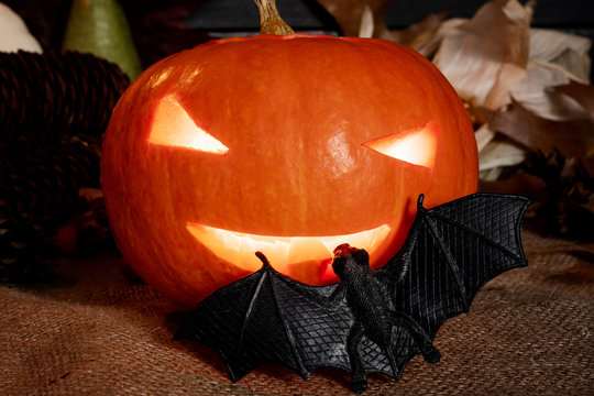 Halloween concept. Carved shining pumpkin with a bat on a jute bag with a background of old planks.