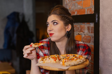 Beautiful and sexy girl sitting by the window in a cafe and eating pizza.