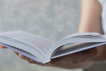 women's hands holding a book in expanded form on a concrete background, the concept of education,...