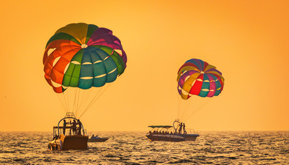 amazing shot at sunset of Parasailing water amusement - flying on a parachute behind a boat on a summer holiday by the sea in the resort Baga beach Goa India India watersports - obrazy, fototapety, plakaty