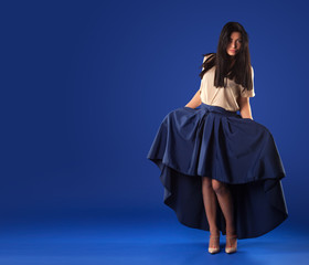 Beautiful brunette woman in a lush long skirt posing on a blue studio background