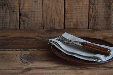 Fototapeta na wymiar Empty clay plate, cutlery, napkin on wooden background. Table setting. Side view. Rustic style. Copy space. Mock up, concept for restaurant, menu