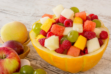 Fruit salad. Peach, watermelon, melon, raspberry, plum, grapes, diced lie in a melon salad bowl on a white wooden background. Whole fruits in wooden spoons. Place for text. Copy space