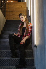 Beautiful and sexy girl posing for a photographer on the black iron stairs with lamps in a cafe.