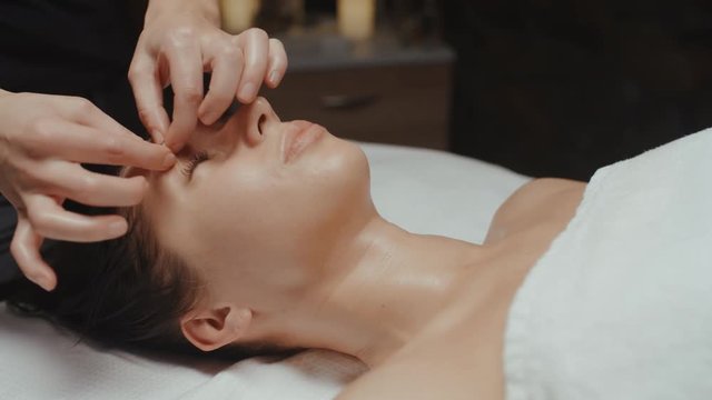 Young caucasian woman receiving facial massage in spa relaxing on massage table. Wellness body and skin care, face treatment, receiving rejuvenation procedure