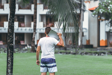 Young freelancer man with laptop in the green tropical park of Bali island.