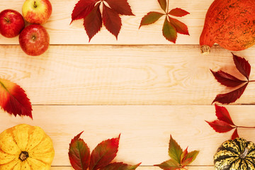 Pumpkins, apples and colorful fallen leaves on a wooden table. Copy space.