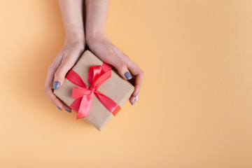 girl holding a present in hands, women with gift box in hands wrapped in decorative paper on a pastel colored background, top view, concept holiday