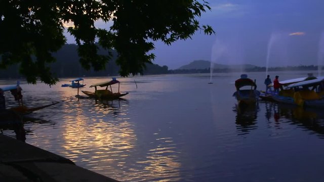 View at a lake with a few boats, people and hill in the background | Dal Lake