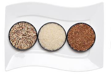 Vegetable food. Macro of a decorative white plate with three bowls with buckwheat, rice and quinoa isolated on a white background. Healthy eating.