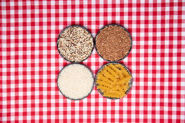 Vegetable food. A frame of four bowls with buckwheat, noodles, rice and quinoa on a red checkered tablecloth. Healthy eating. Top view with space for product montage.