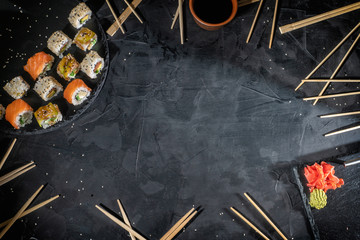 Frame made delicious sushi rice rolls on black stone plate with soy sauce and chopsticks. Space for text, top view © Andrii