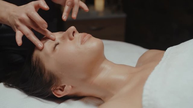 Facial massage in spa relaxing on massage table. Caucasian woman receiving wellness body and skin care, face treatment, receiving rejuvenation procedure