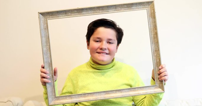 Portrait of a handsome young boy  looking through emty frame and making silly faces to a camera