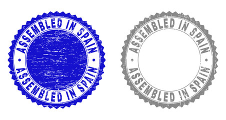 Grunge ASSEMBLED IN SPAIN stamp seals isolated on a white background. Rosette seals with distress texture in blue and gray colors.