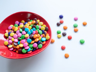 Multicolored chocolate beans in a bowl and side on a white background