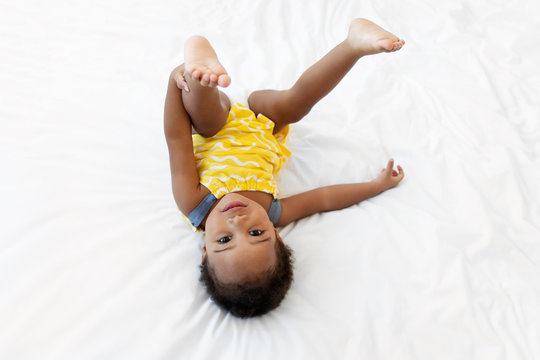 Toddler girl holds her leg upside down on bed