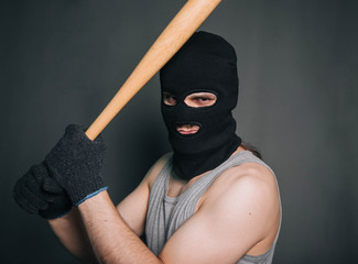 Bandit, the criminal in a black mask and in a gray T-shirt with a painless bat. Robber with a weapon. A man in a balaclava and a gray mask on a gray background