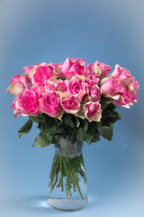 Bouquet of pink roses in a glass vase on a blue background