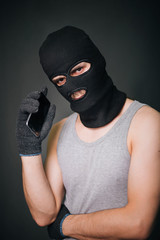 The criminal in a black mask with a smartphone. a guy in a balaclava and a cell phone. The criminal is negotiating
