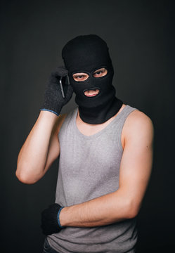 The criminal in a black mask with a smartphone. a guy in a balaclava and a cell phone. The criminal is negotiating