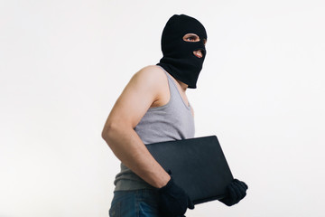A thief in a black mask stole a laptop. A man in a balaclava and with a computer in hands on a...