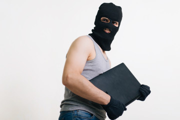 A thief in a black mask stole a laptop. A man in a balaclava and with a computer in hands on a...