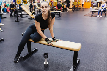 Portrait of a beautiful elegant young slim woman fitness blogger sitting on a sport bench and resting after a workout. The concept of a healthy lifestyle and physical activity in the gym