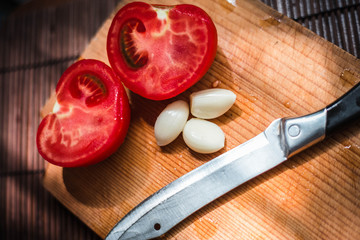 Wooden board for cooking and knife. Sliced tomatoes with garlic