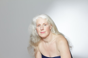 Headshot of an attractive mature woman with beautiful long gray hair in front of white background, copy space.