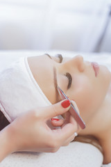 Eyelash Extension Procedure. Woman Eye with Long Eyelashes. Beautiful young girl  tweezing her eyebrows in a beauty salon. Eyebrow Correction. Beauty Concept. Permanent Makeup. Microblading brow.