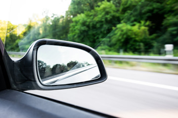 Car rear-view mirror on the motorway in summer in Germany with green trees in the background