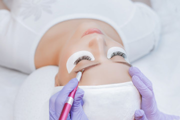 Naklejka premium Beautiful young girl with long eyelashes tweezing her eyebrows in a beauty salon. Eyebrow Correction. Beauty Concept. Permanent Makeup. Microblading brow. Beautician Doing brows Tattooing.