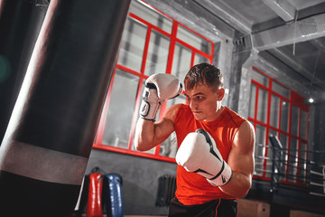 Killing workout. Muscular boxer with white boxing gloves in safeguard stand on red window background